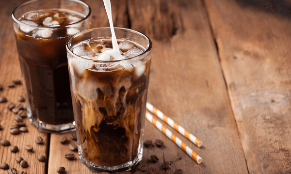 Two glasses with ice coffee on a wooden table with straws next to them