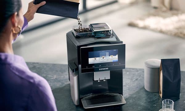 Kvinne fyller opp bønnebeholderen på en Siemens kaffemaskin