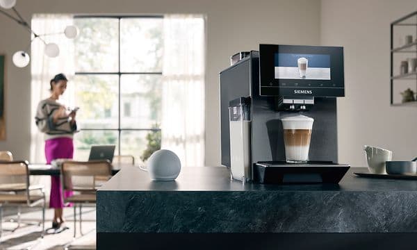 Siemes EQ900 kaffemaskin på kjøkkenbenk ved siden av smartøyttaler med kvinne i bakgrunnen