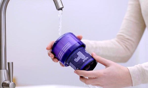 Henkilö huuhtelee Dyson-varsipölynimurin suodatinta lämpimällä vedellä