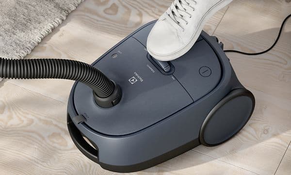 Electrolux Clean 600 støvsuger i pose i grå og en menneskefot som bruker fotkontrollen
