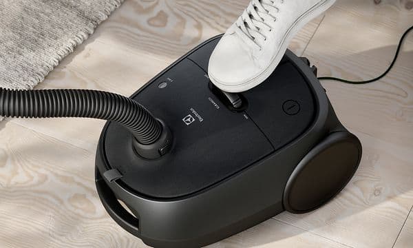Electrolux Clean 600 støvsuger i pose i svart og en menneskefot som bruker fotkontrollen