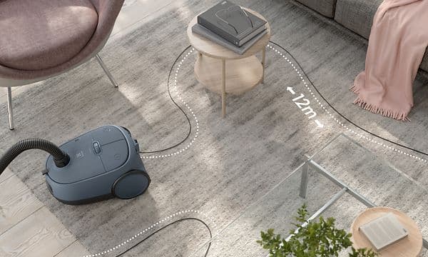 Grå Electrolux Clean 600 Støvsuger med pose i stuen og illustrasjon som viser dens 12 meter radius