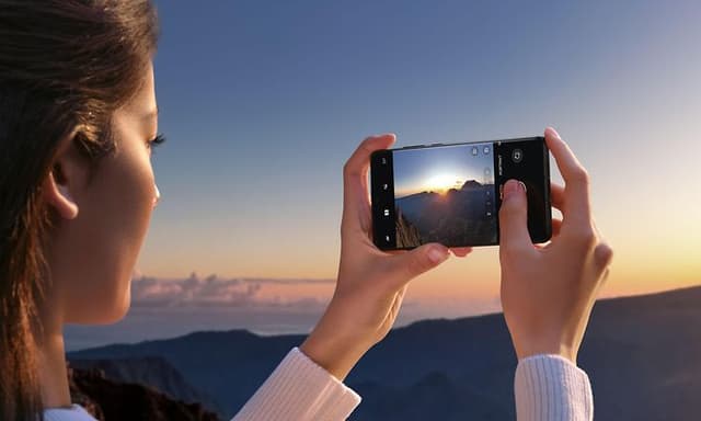 OnePlus 12 - nainen ottaa auringonlaskusta valokuvan OnePlus 12 -älypuhelimella