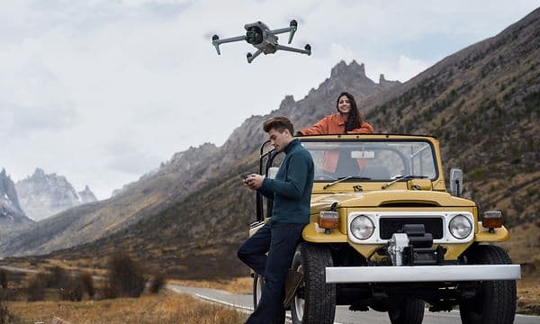 En man som flyger en DJI Air 3 ståendes bredvid en bil
