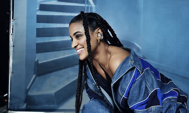 CE - Bose Ultra Open Earbuds - En kvinde, der har Bose Earbuds i ørerne på en blå baggrund