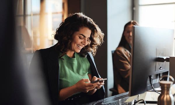 Digital cleanup - Kvinde med en smartphone foran en PC på et kontor