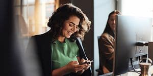 Digital cleanup - Kvinde med en smartphone foran en PC på et kontor