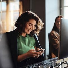 Digital cleanup - Woman with a smartphone in front of a PC in an office