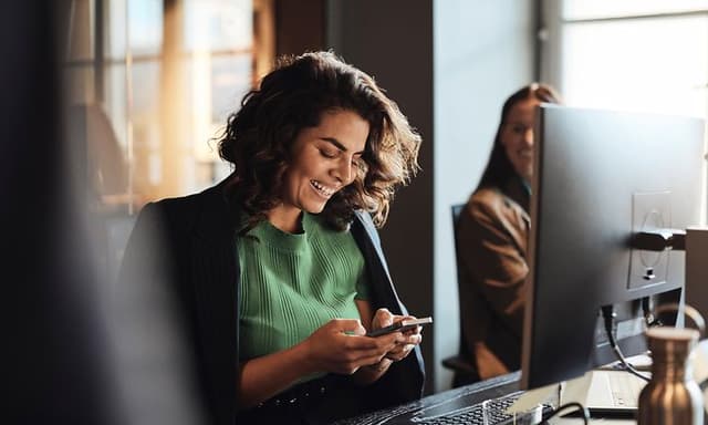 Digital cleanup - Woman with a smartphone in front of a PC in an office