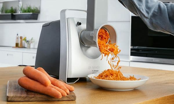 Person using Bosch meat grinder's shredding attachment to grate carrots