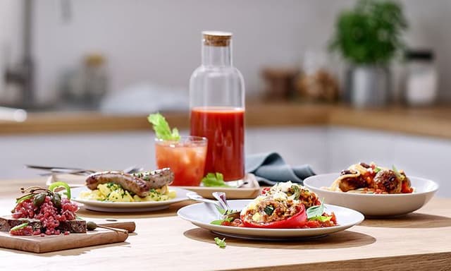 A bottle with smoothie and several dishes of food on the kitchen table