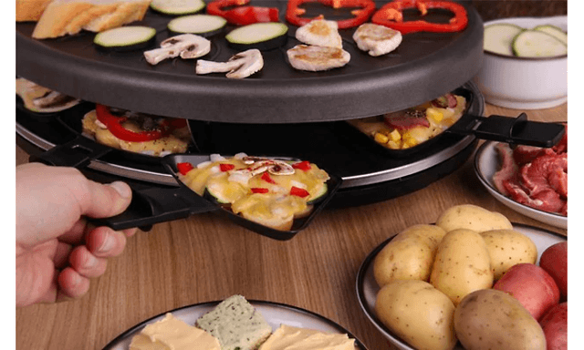 Person som plasserer raclette-jern i en raclette med mat