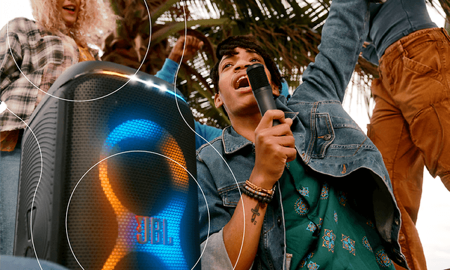 Young man singing to a microphone that is connected to JBL Partybox Stage speaker