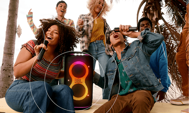 Woman and man singing to microphones while sitting next to JBL Partybox Stage 120 speaker