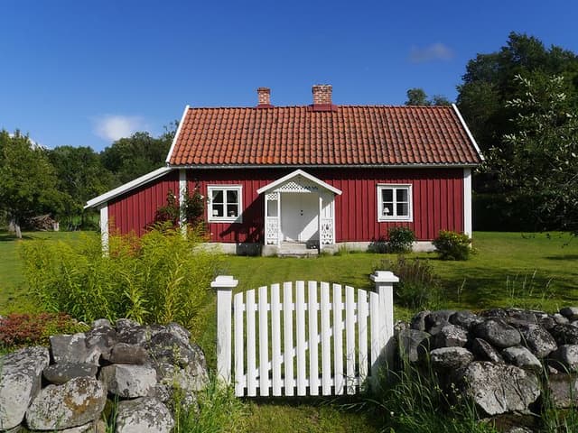 en vit grind som leder in till en stuga målad i falurödfärg