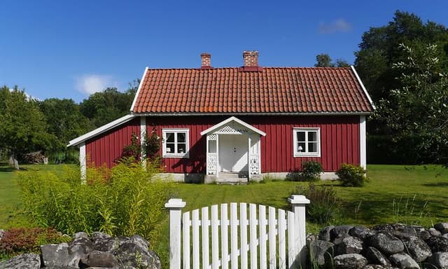 en vit grind som leder in till en stuga målad i falurödfärg