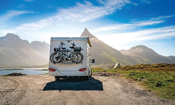 Bobil som står parkert ved et vann, fjell i bakgrunnen