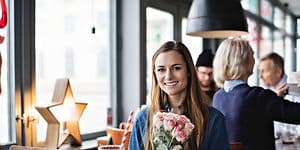 Giv glæde på mors dag: Kvinde på café med blomster og gaver omkring sig