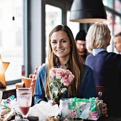 Woman in cafe with flowers and gifts around her