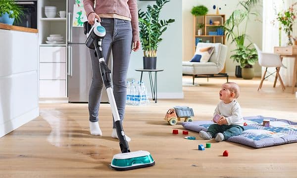 En mor som bruker en Bosch-støvsuger som vasker gulvet samtidig ved siden av en baby