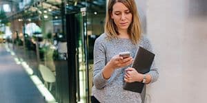 Woman leaning against office wall while checking her phone
