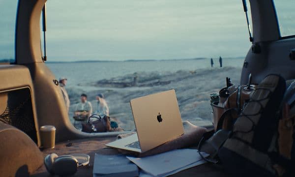 En åben MacBook Air i bagklappen på en bil med en strand i baggrunden