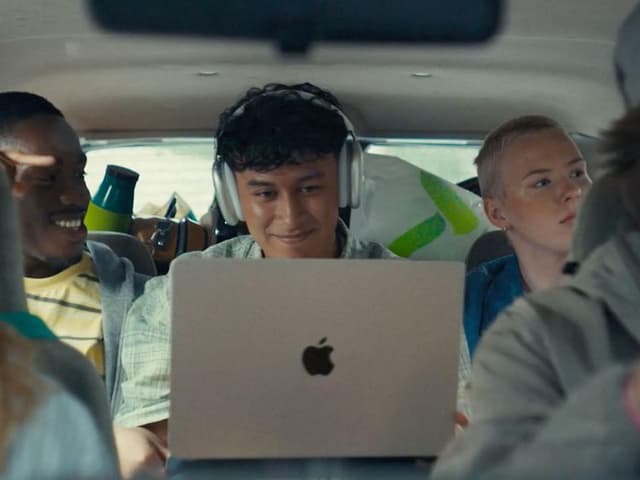 Ung studerende på bagsædet af en bil med MacBook Air på skødet og AirPods Max på