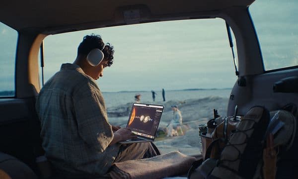 En ung mann sitter med Airpods Max på og studerer med en MacBook Air på fanget
