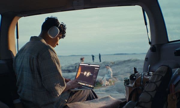 Gutt som bruker en mac og airpods max i en van