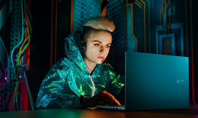 Pimeässä istuva tyttö työskentelee ASUS Vivobook 16X K3605Z kannettavalla tietokoneellaan
