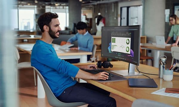 Hymyilevä mies työskentelee toimistossa HP EliteBook -kannettavalla