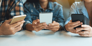 tre ungdommer bruker smarttelefon ved et bord