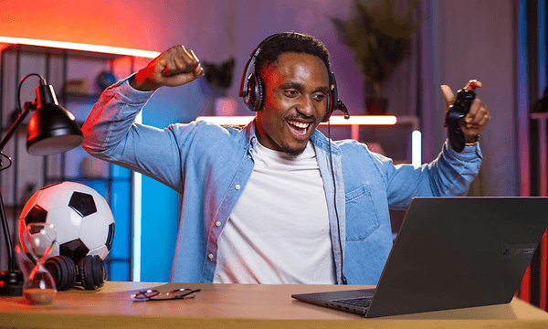 Man cheering in front of a Asus Vivobook 16X K3605Z laptop and a football next to him