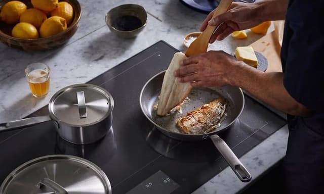 An All Steel Fiskars frying pan on an induction hob, cooking a fillet of fish to crispy perfection.