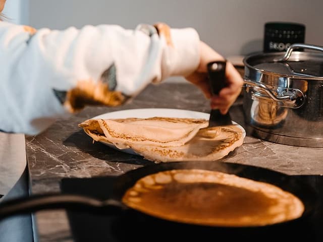 A frying pan with golden pancakes cooking on an induction hob, evenly heated on the modern stovetop