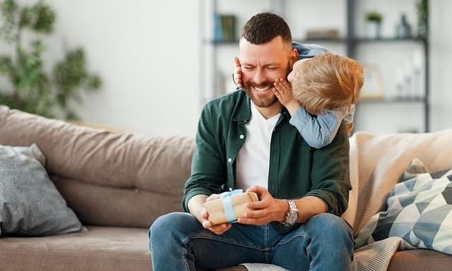 Mies istuu sohvalla ja saa lahjan pieneltä pojaltaan