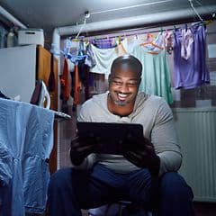 Man sitting with tablet in laundry room having some me-time