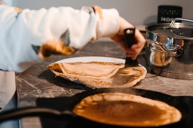 En stegepande med gyldne pandekager tilberedt på en induktionskogeplade, jævnt opvarmet på det moderne komfur