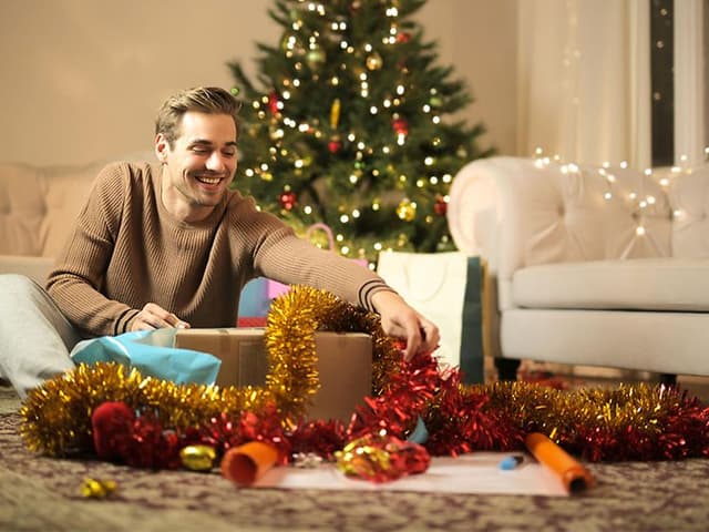 Man opening presents in front of a Christmas tree