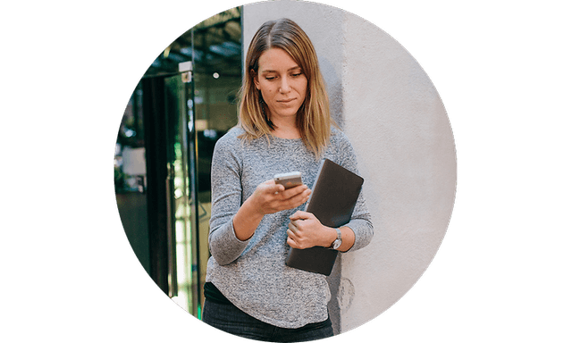 Kvinne holder sin laptop mens hun jobber med mobilen sin