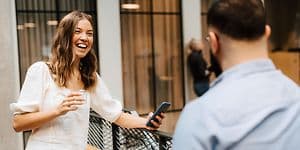 Smilende kvinde med sin arbejdstelefon i hånden taler med kollega på kontor 