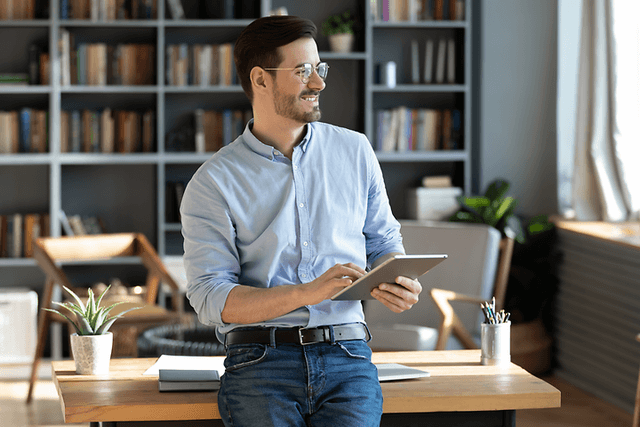 B2B - CS - Smiling man standing next to a desk holding a tablet