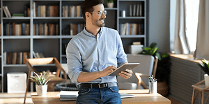 B2B - CS - Smiling man standing next to a desk holding a tablet
