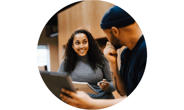 Man holding an open laptop while discussing with a woman