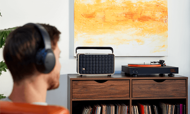 Pladespilleren JBL SPINNER på reol og en mand, som lytter til musik via trådløse hovedtelefoner