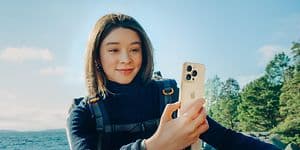 iPhone 16 Pro i hånden på en kvinde, som står i naturen