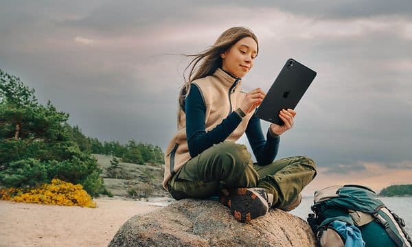 Kvinne som sitter på en stein på stranden med en iPad