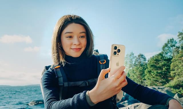 Kvinne med ryggsekk som holder en iPhone 16 Pro