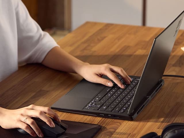En person bruker ASUS TUF Gaming A14 på et skrivebord av tre